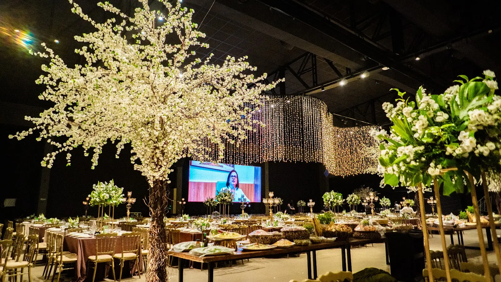 Salão decorado com árvores floridas e mesas montadas para o Encontro de Corretores