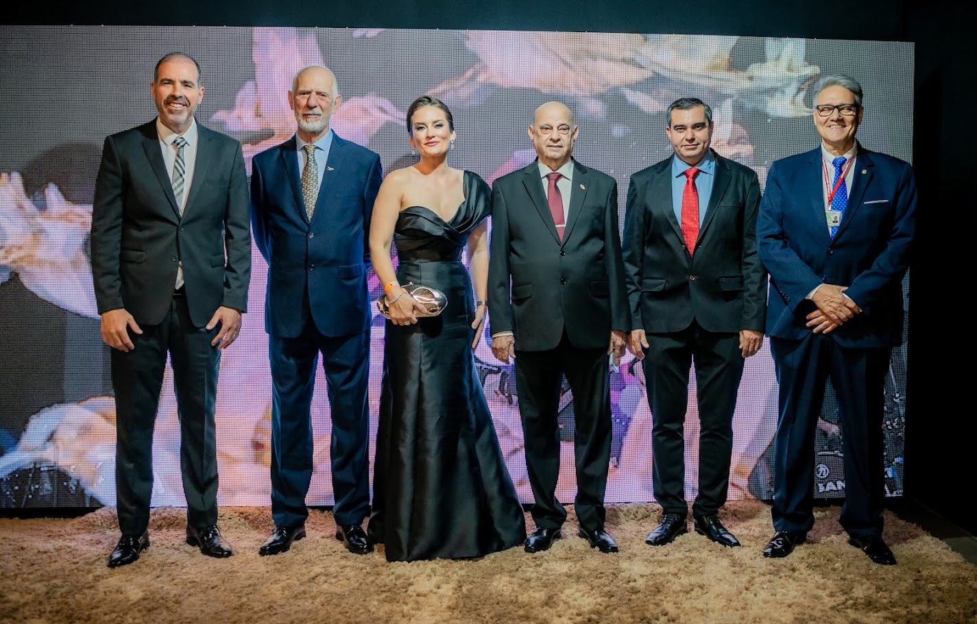 Homenageados posando no painel de LED do evento